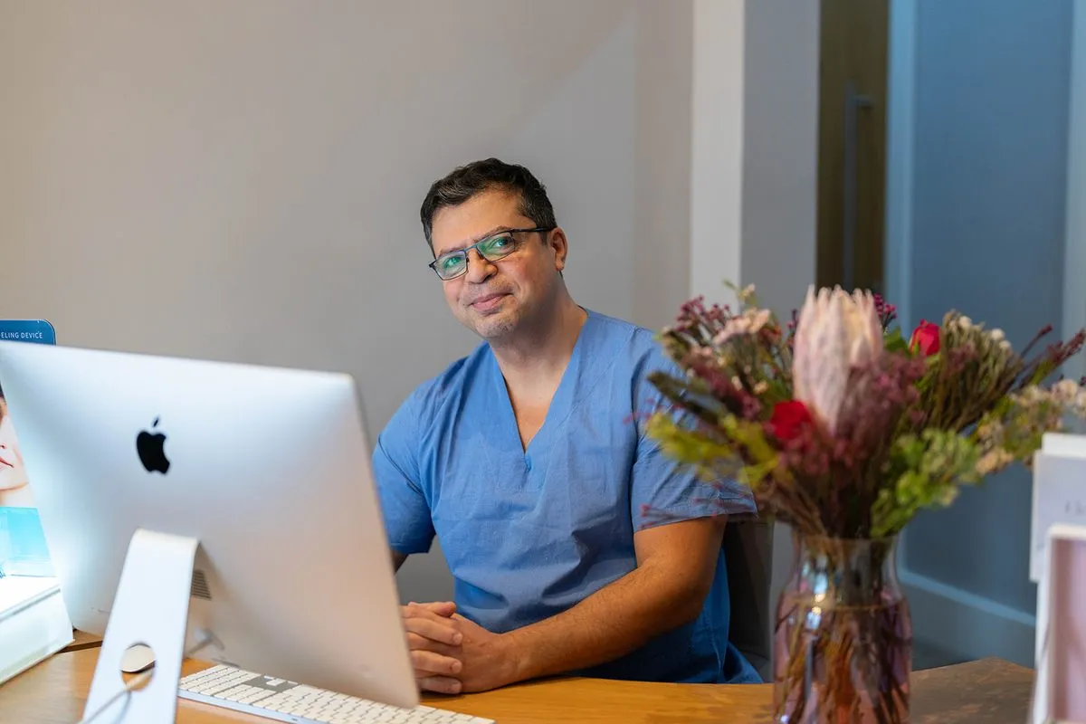 Dr Shahe Boghossian, Medical Consultant, in blue scrubs at a desk in The London Road Clinic, Newark.