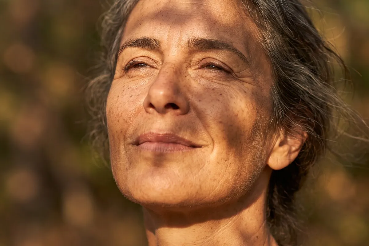 Daylight portrait, a woman in her forties, dappled leaf shadow falling across the face and neck.