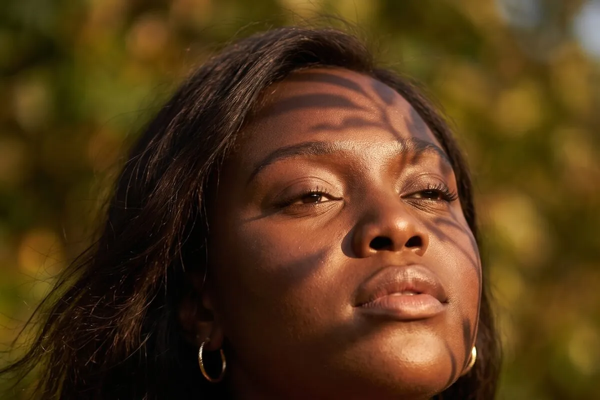 Daylight portrait, a woman in her twenties with long dark hair, eyes half closed, dappled leaf light across the face.