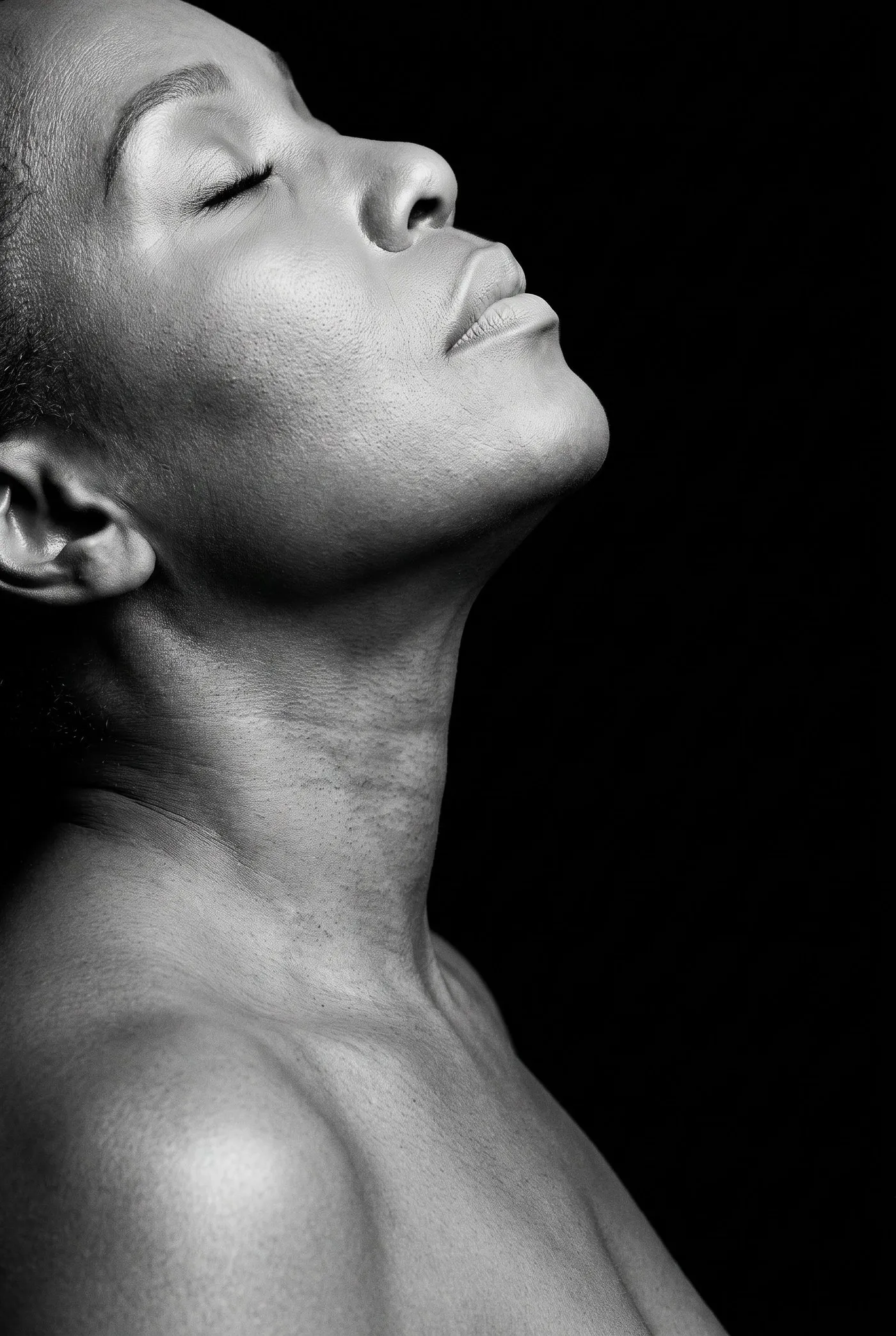 Black and white studio photograph, a woman in her fifties, neck and collarbone against a dark ground.